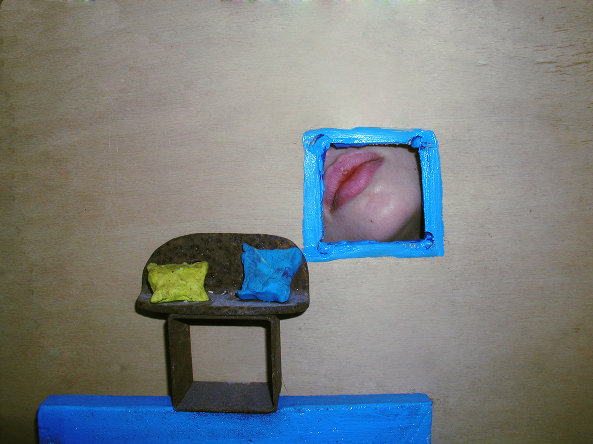 Mixed media werk 'Fantastisch landschap 3': een klein bankje met een geel en blauw kussen tegen een houten muur, met daarnaast een blauw geschilderd venster waarin een mond zichtbaar is.