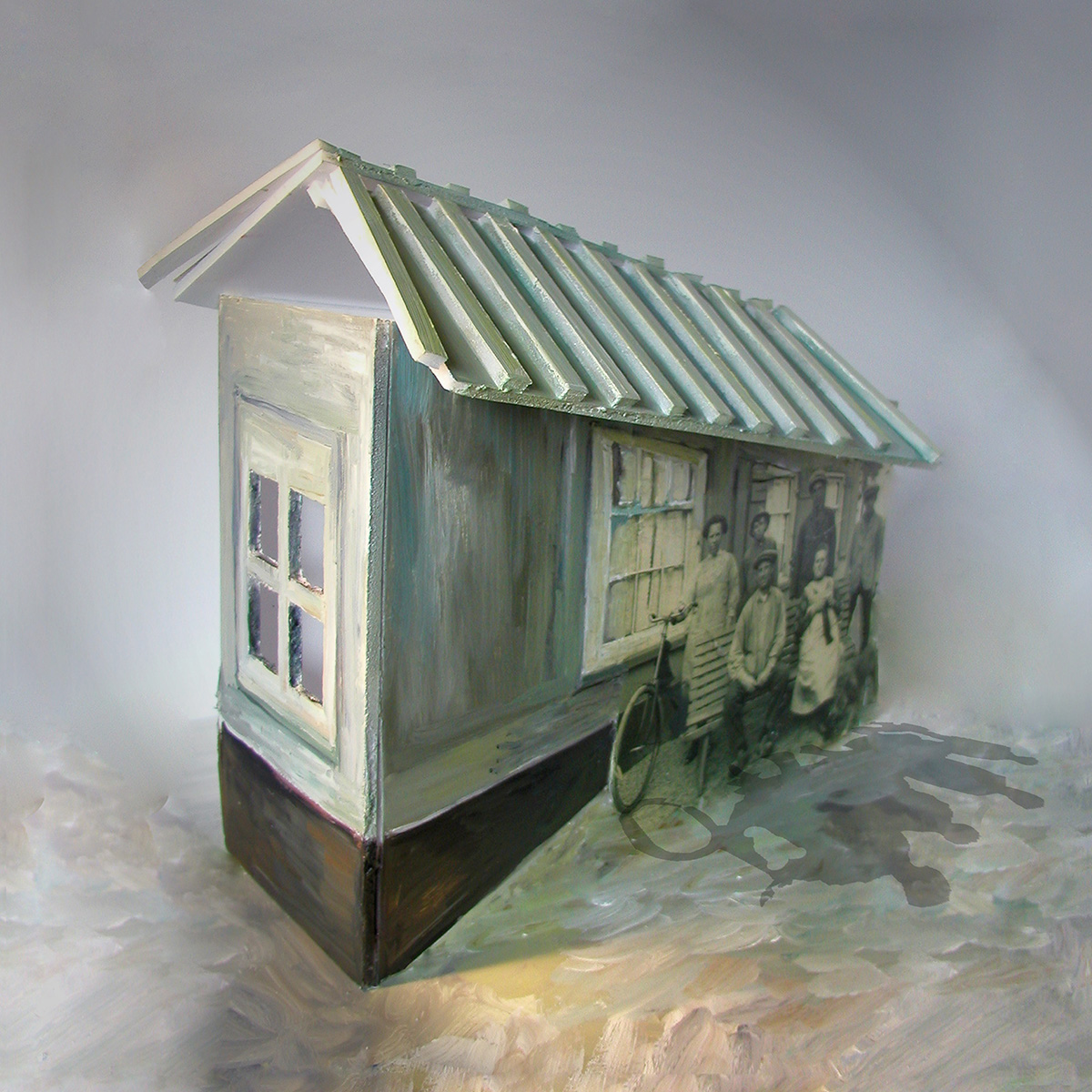 Mixed media werk 'Tijd 1': een beschilderd miniatuurhuisje met een dak van foam, waarin een oude zwart-witfoto van een gezin met fiets voor de gevel is verwerkt.